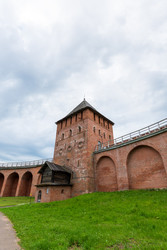 великий новгород, россия. дворцовая башня новгородского кремля, крепость из красного кирпича с арочными проемами и крутой шатровой крышей, видимая со склона в пасмурном летнем свете - NikitaMaykov