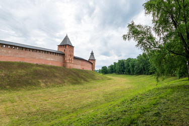 великий новгород, россия. стены новгородского кремля и княжая башня, крепостная архитектура из красного кирпича с высокой шатровой крышей, панорамный летний вид под облачным утренним небом - NikitaMaykov