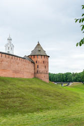 великий новгород, россия. митрополичья башня новгородского кремля, крепостная стена из красной кладки и круглое оборонительное сооружение с деревянной крышей, вид с зеленой набережной при мягком летнем освещении - NikitaMaykov