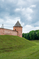 великий новгород, россия. федоровская башня новгородского кремля с цилиндрическими кирпичными стенами, конической деревянной крышей, средневековой крепостной архитектурой и зеленым ландшафтом крепостного вала под пасмурным летним небом - NikitaMaykov