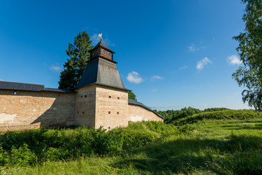 печоры, псковская область, россия. благовещенская башня псково-печерского монастыря, каменные крепостные стены и деревянная крыша под ясным голубым небом, вид летним утром - NikitaMaykov