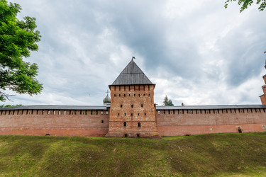 великий новгород, россия. покровская башня новгородского кремля, крепостная стена из красного кирпича с высокой пирамидальной крышей, прямоугольное средневековое сооружение и панорамный вид снаружи - NikitaMaykov