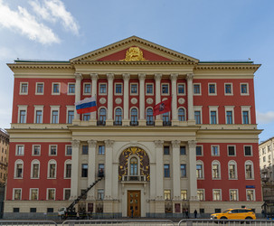 москва, россия - 10.01.2026: мэрия москвы на тверской, 13 с флагами россии и москвы, кремовыми колоннами, красным фасадом, голубым небом - Sadoff