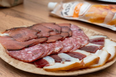 крупно нарезанное мясное ассорти, включая копченый бекон, колбасу салями, прошутто и вяленое мясо, подается на круглой деревянной доске - DmitryKurullin
