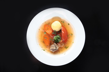 перелейте мясной бульон в белую миску. картофель, морковь, помидор, петрушка, кусочки говядины. вид сверху. полезный домашний суп на темном фоне - RusAKphoto