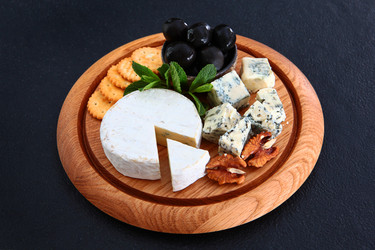 сырная доска с сыром бри, кубиками голубого сыра, крекерами, маслинами, грецкими орехами, мятой на круглом деревянном блюде. темный фон - RusAKphoto