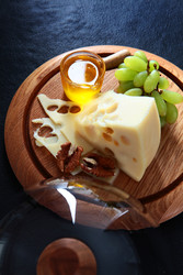 сыр с дырочками, зеленый виноград, банка с медом, грецкие орехи, деревянная доска, перевернутый стеклянный клош на темном фоне - RusAKphoto