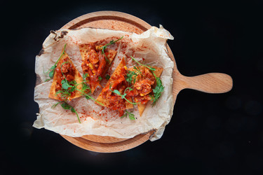 мексиканская закуска начос с томатным соусом и зеленью. треугольные начос с томатным соусом и зеленью выложите на пергаментную бумагу. вид сверху. деревянная доска на темном фоне - RusAKphoto