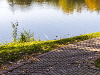 • Paved park walkway along a quiet pond bank with fishing rods. Hobby - Pazemin