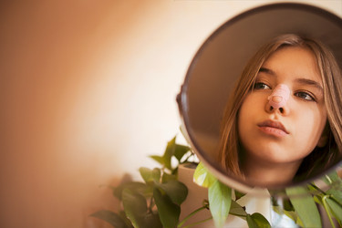 молодая женщина, отражающаяся в круглом зеркале в окружении зеленых листьев комнатных растений, теплый естественный свет и мягкая нейтральная стена, созерцательная портретная сцена в помещении - Darya Petrenko