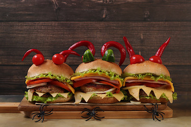 Horrible hamburgers with fresh lettuce, tomatoes, cream cheese, salad, onion, cutlets and peppers in the shape of horns on an old wooden background. Halloween food concept, cafe advertising - svetlanabalyn