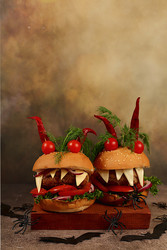 Scary hamburgers with fresh lettuce, tomatoes, cream cheese, lettuce, onions, cutlets and peppers in the form of horns on an old concrete background, cafe advertising, menu, restaurant business card - svetlanabalyn