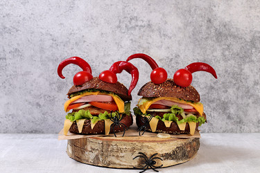 Halloween food concept. Scary hamburgers with fresh lettuce, tomatoes, cream cheese, lettuce, onions, cutlets and peppers in the form of horns on an old concrete background, cafe advertising, menu, - svetlanabalyn