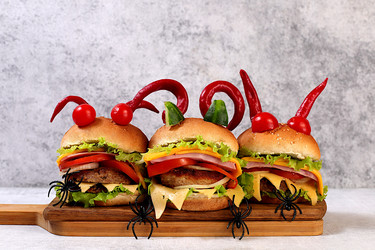 Halloween food concept. Scary hamburgers with fresh lettuce, tomatoes, cream cheese, lettuce, onions, cutlets and peppers in the form of horns on an old concrete background, cafe advertising, menu, - svetlanabalyn