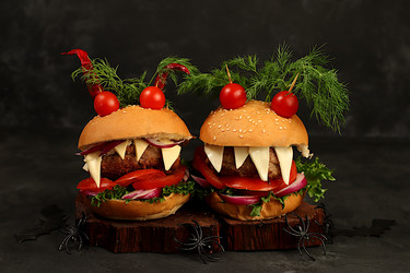Halloween food concept. Scary hamburgers with fresh lettuce, tomatoes, cream cheese, lettuce, onions, cutlets and peppers in the form of horns on an old concrete background, cafe advertising, menu - svetlanabalyn