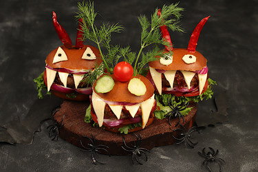 Halloween food concept. Scary hamburgers with fresh lettuce, tomatoes, cream cheese, lettuce, onions, cutlets and peppers in the form of horns on an old concrete background, cafe advertising, menu, - svetlanabalyn