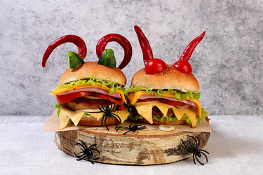 Scary hamburgers with fresh lettuce, tomatoes, cream cheese, lettuce, onions, cutlets and peppers in the form of horns on an old concrete background, cafe advertising, menu, restaurant business card, - svetlanabalyn