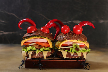 Horrible hamburgers with fresh lettuce, tomatoes, cream cheese, salad, onion, cutlets and peppers in the shape of horns on an old concrete background. Halloween food concept, cafe advertising, menu - svetlanabalyn