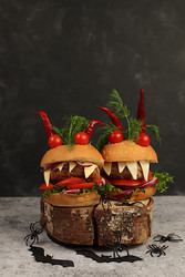 Horrible hamburgers with fresh lettuce, tomatoes, cream cheese, salad, onion, cutlets and peppers in the shape of horns on an old concrete background. Halloween food concept, cafe advertising, menu - svetlanabalyn