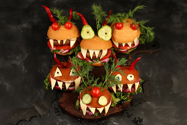 Halloween food ideas. Horrible hamburgers with fresh lettuce, tomatoes, cream cheese, lettuce, onion, cutlets and peppers in the shape of horns on an old concrete background. Halloween food concept, - svetlanabalyn