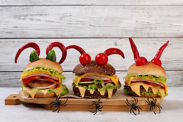 Horrible hamburgers with fresh lettuce, tomatoes, cream cheese, salad, onion, cutlets and peppers in the shape of horns on an old wooden background. Halloween food concept, cafe advertising - svetlanabalyn
