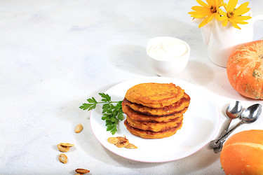 натуральная веганская еда.вкусные вегетарианские блинчики в русском стиле, блинчики с тыквой, тыквенными семечками и петрушкой, подаются с порцией сметаны на кухонном столе, концепция здорового питания, - svetlanabalyn