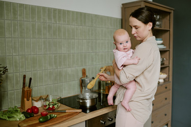Мать держит ребенка на руках во время приготовления еды на кухне у себя дома - AnnaStills