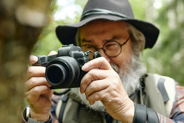 Пожилой мужчина фотографирует на камеру в лесу - SeventyFour