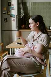 Усталая мать держит на руках спящего ребенка и пьет кофе дома - AnnaStills