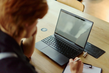 Женщина работает за ноутбуком и делает заметки за офисным столом - DragonImagesAsia