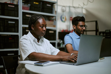 Чернокожая женщина работает за ноутбуком с коллегой в офисе склада - DragonImagesAsia