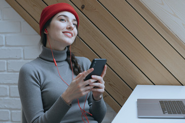Женщина слушает музыку в наушниках на смартфоне в помещении - SeventyFour